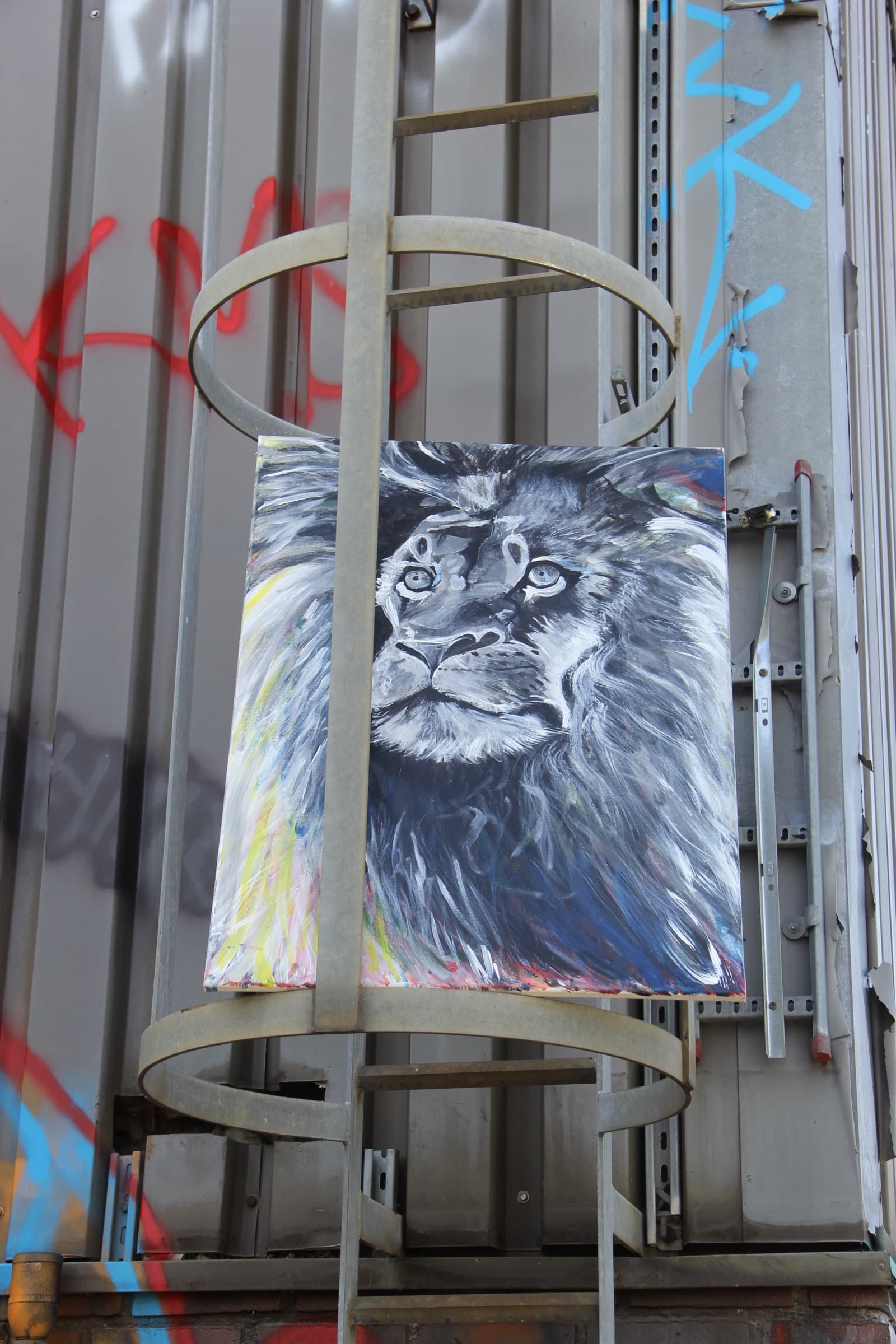 The lion painting held upright in a metal ladder cage on a corrugated shipping container marked with red and blue spray tags